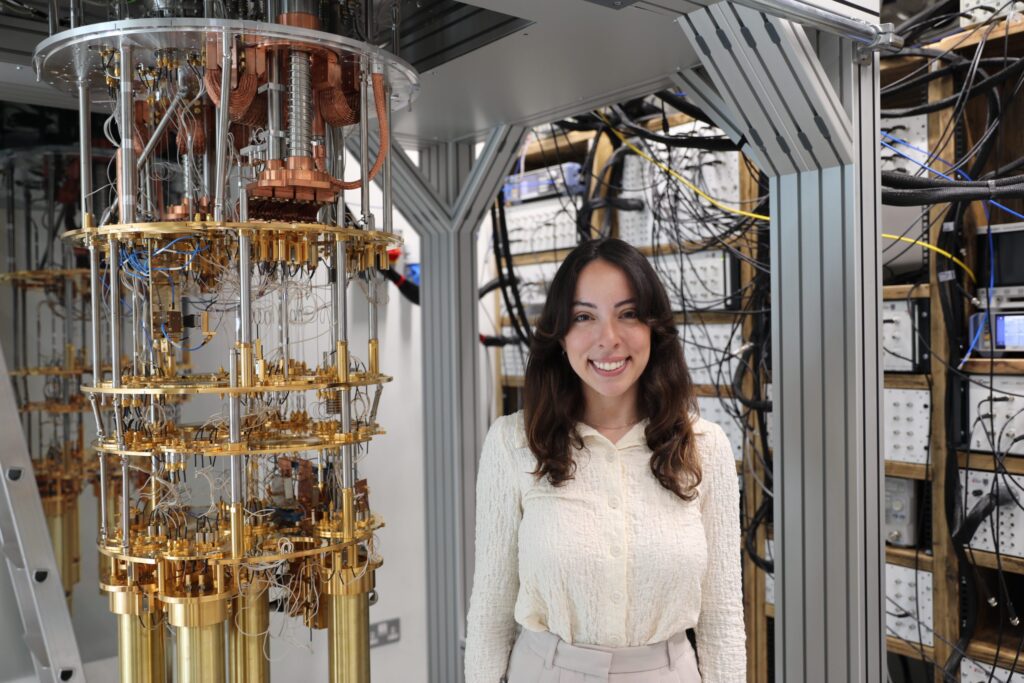 April Carniol of Motion Quantum standing in front of an array of electronic equipment.