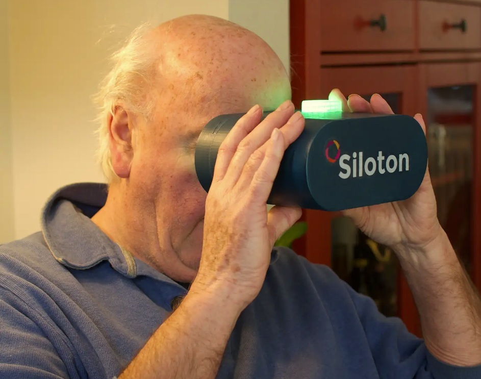 A man holds a headset up to his face, covering his eyes. The headset says Siloton across the front.