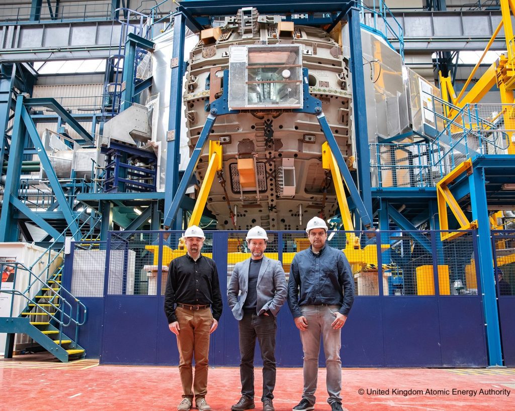 Saman Ghannadzadeh, Anthony Laing and Fazal Chaudry, wearing hard hats and standing in front of a large piece of factory machinery.