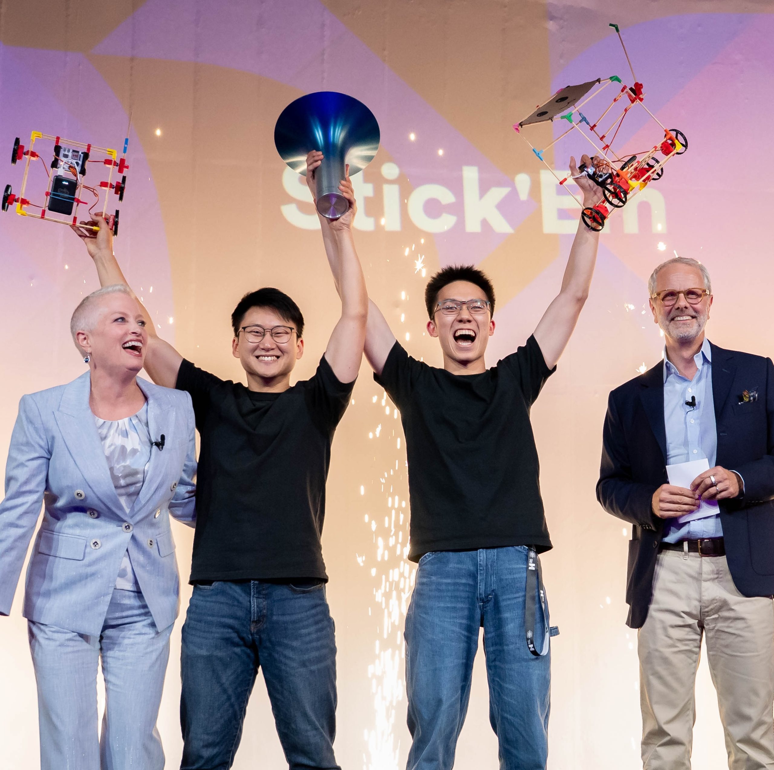 Four people stand on a stage, the middle two cheering. The woman on the left is Lori van Dam.