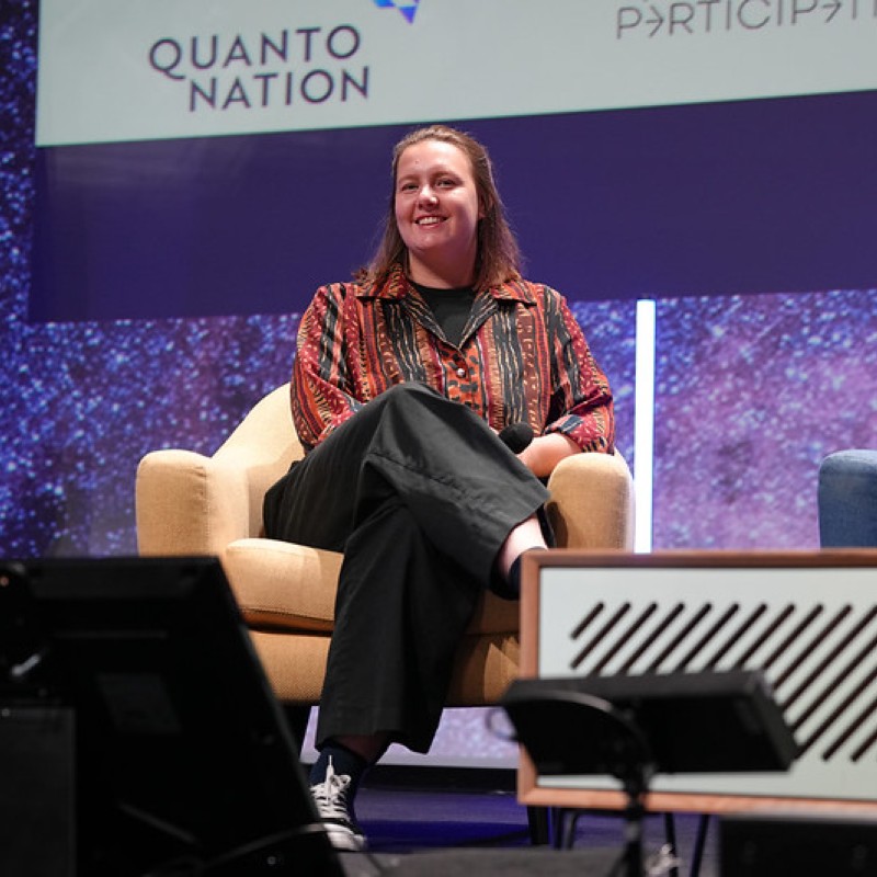 Emily Meads, principal at Quantonation, sitting on a chair on stage at an event.