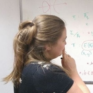 A headshot of Chloe Martindale, turned away from the camera looking at a whiteboard covered in equations.